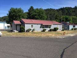A public housing duplex with large trees in the background and a street in front.